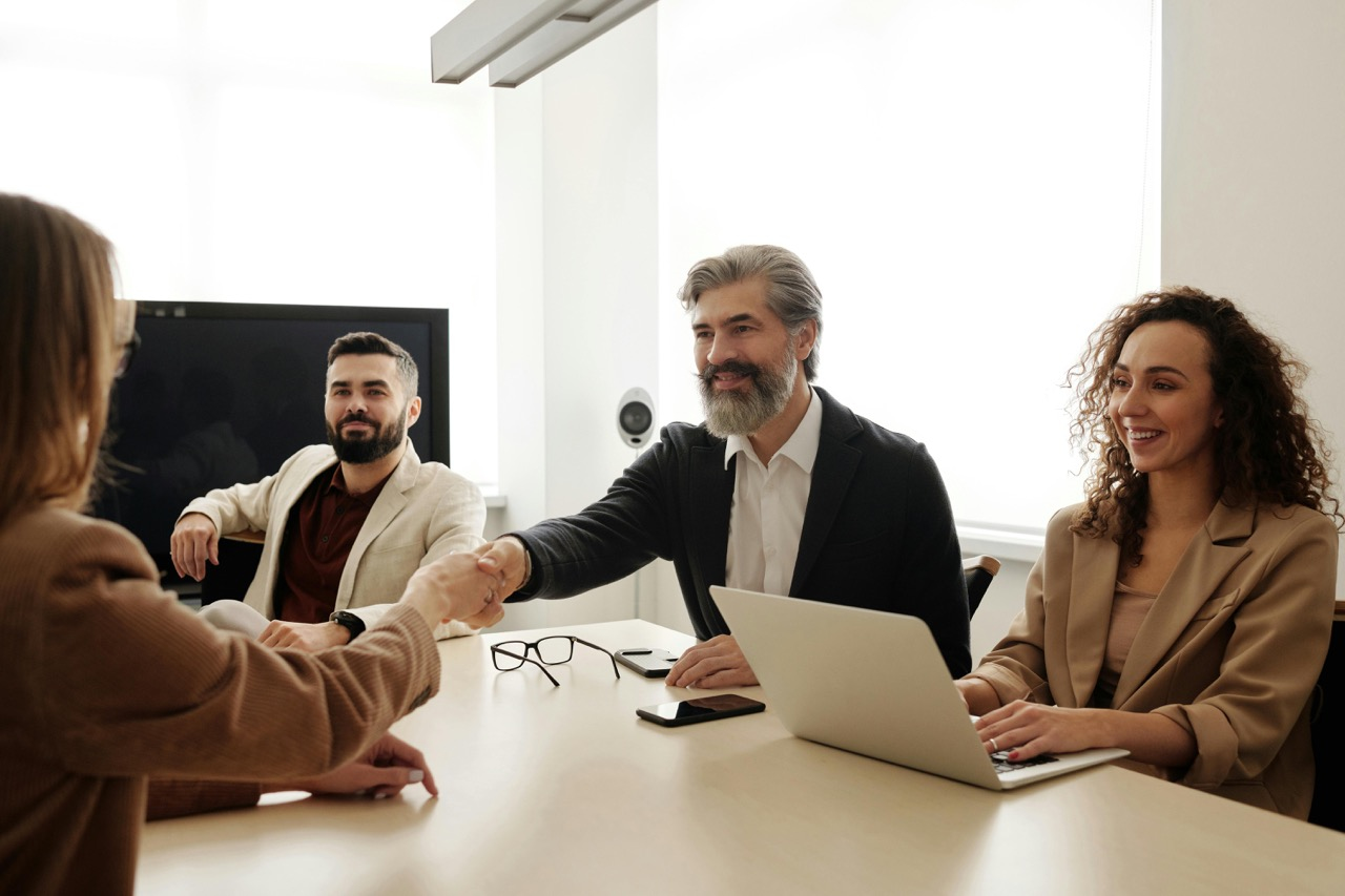 A group of business professionals in a meeting room, with one person shaking hands across the table, symbolizing agreement or a successful negotiation.