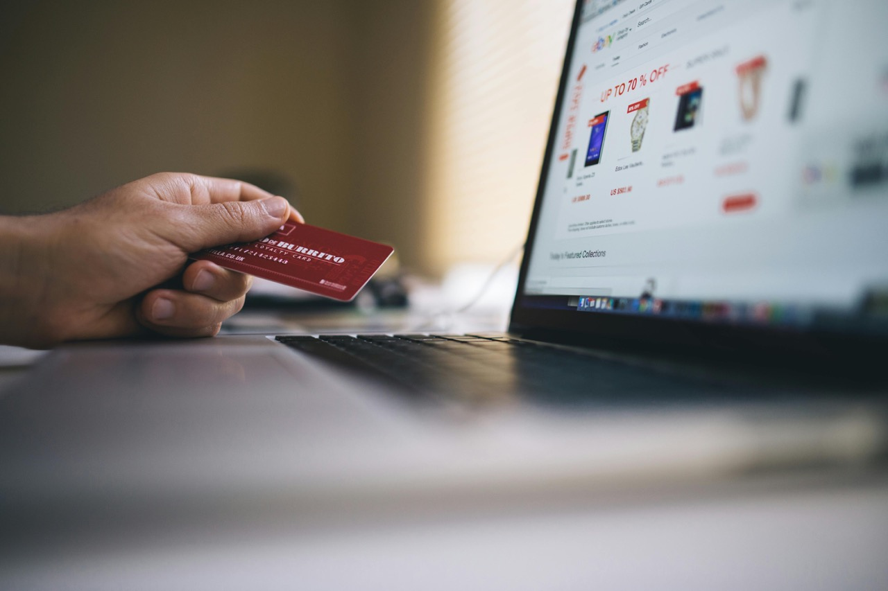 Person holding a credit card while shopping online on a laptop, with a webpage displaying various items on sale.