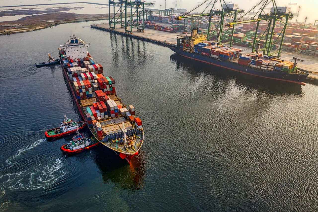 A large container ship being assisted by tugboats as it enters a busy port